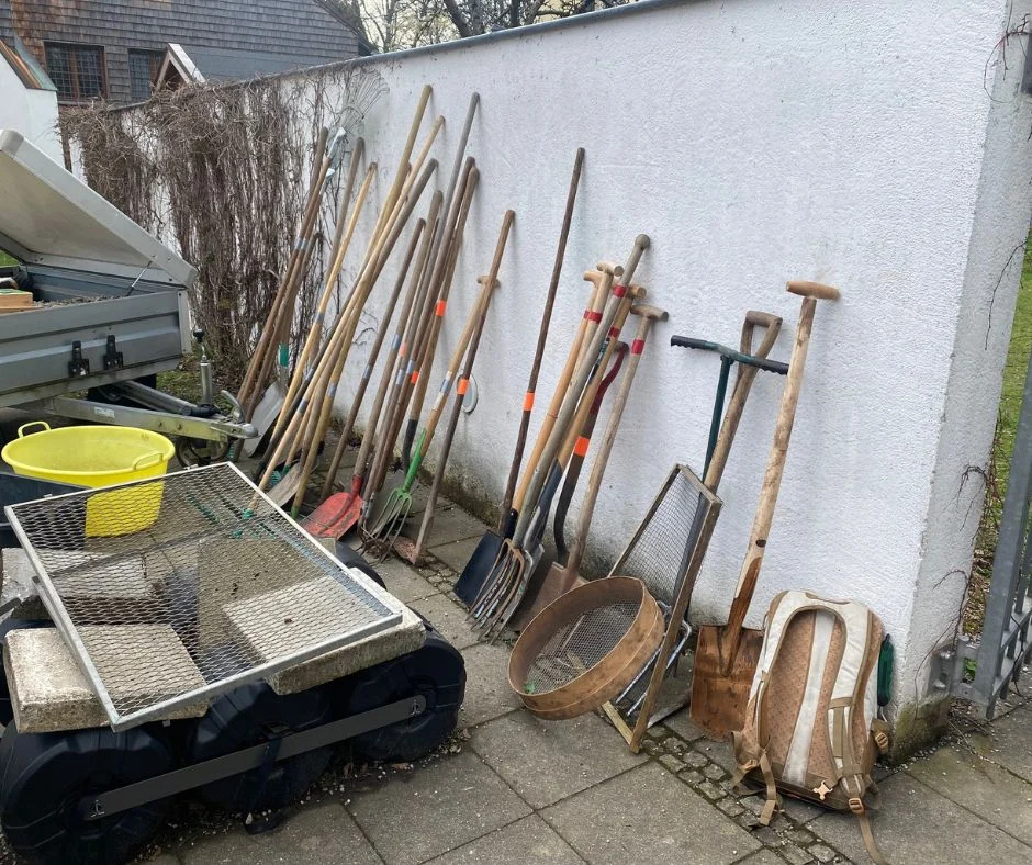 Spaten, Rechen und andere Gartengeräte lehnen an einer Hauswand