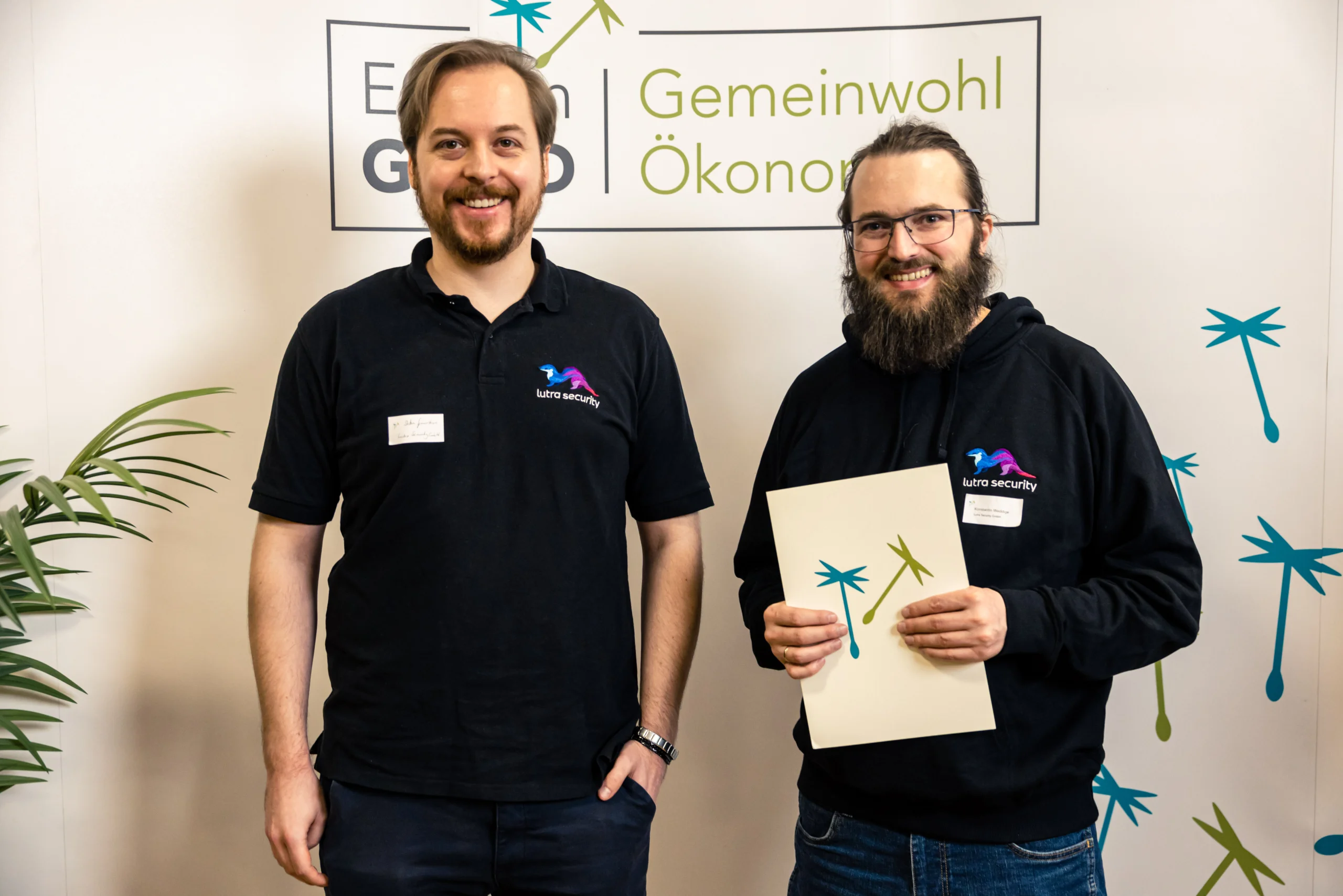 Zwei Männer mit einer Urkunde vor einer Wand der Gemeinwohl-Ökonomie