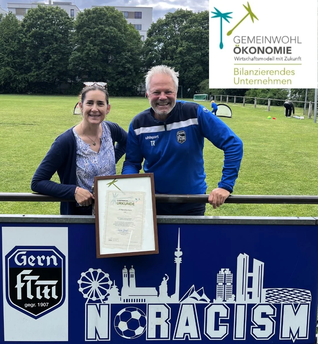 Zwei Personen mit Urkunde auf einem Sportplatz vor einem Banner