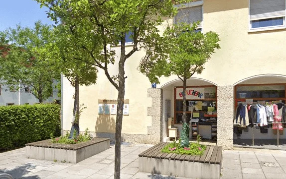 Platz mit Bäumen und Pflanzkübeln vor einer Häuserzeile mit Arkaden
