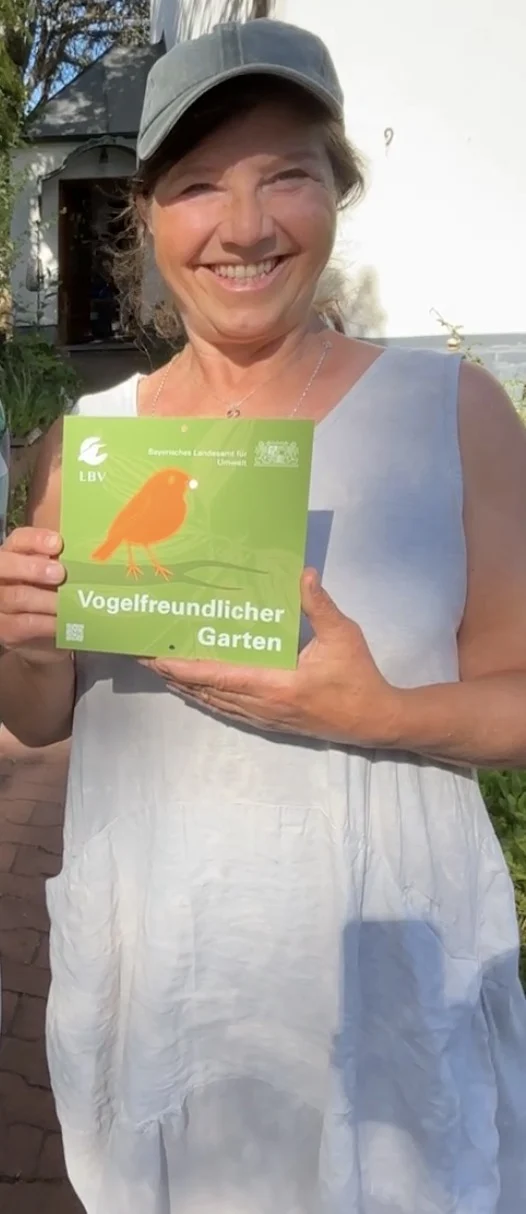 Screenshot Frau mit Kappe hält ein grünes Blatt Papier in die Kamera