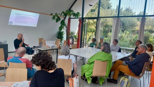 Menschen sitzen an Tischen in einem hellen Raum bei einer Präsentation