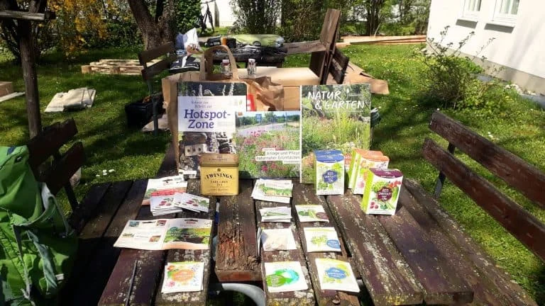 Infostand mit Pflanzen und Broschüren auf einem Holztisch im Garten