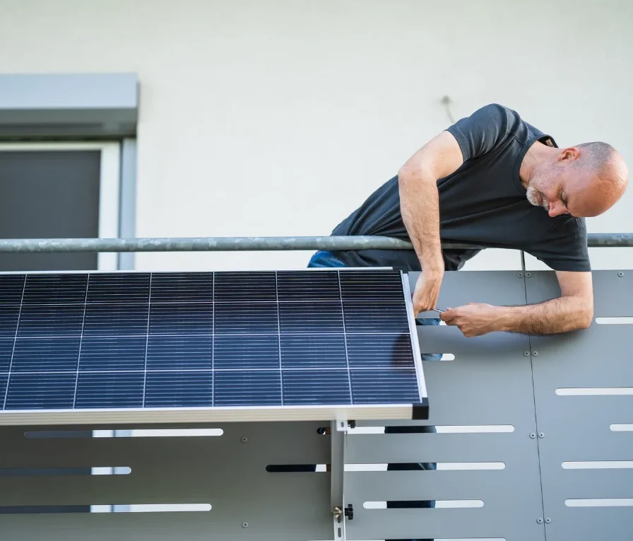 Mann montiert ein Solarmodul an einem Balkon